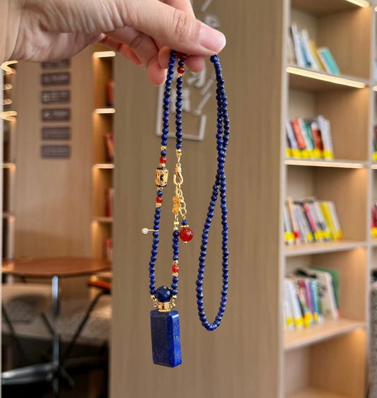Close-up of a hand unscrewing the gold-plated cap of a lapis lazuli perfume bottle pendant.