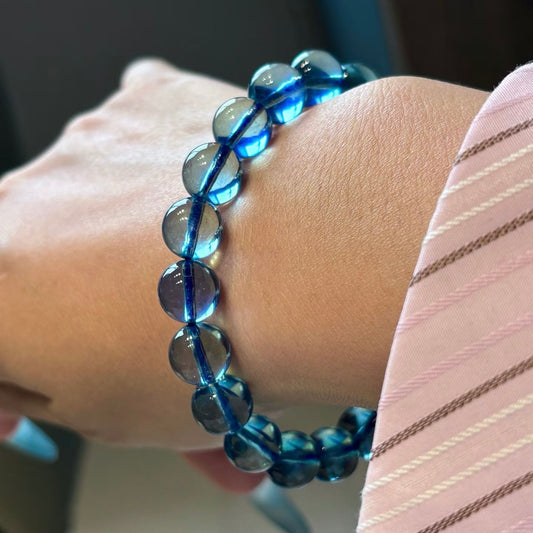 Macro photography of a high-definition, glass-body natural aquamarine bead bracelet on a woman's wrist, showing intense deep sea blue light refraction against the skin.