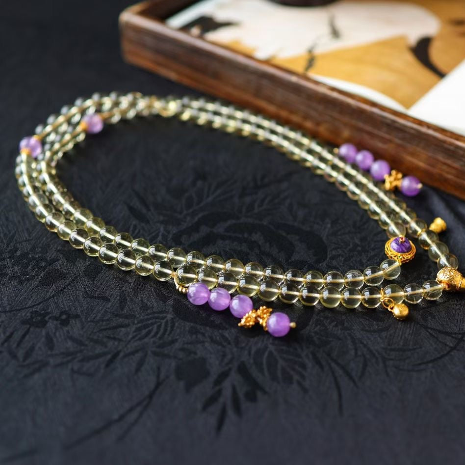 High-clarity 8mm citrine 108 mala beads displayed on a dark embroidered fabric.