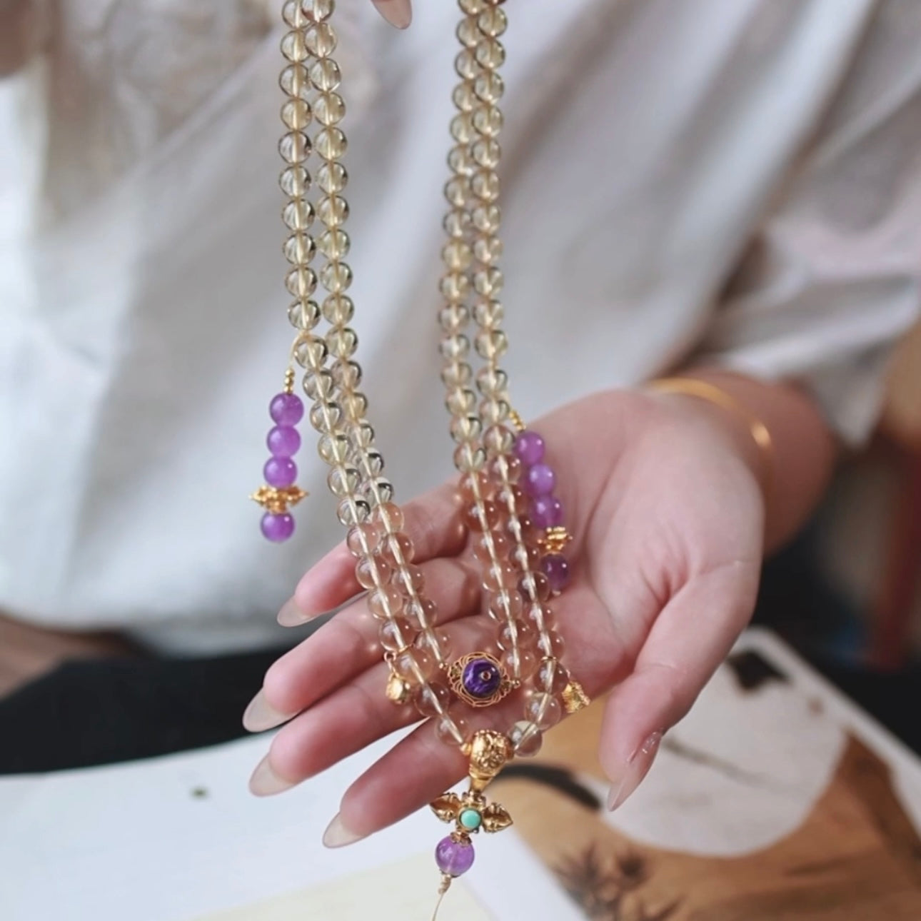 The citrine mala beads wrapped around a model's wrist as a bracelet during meditation.