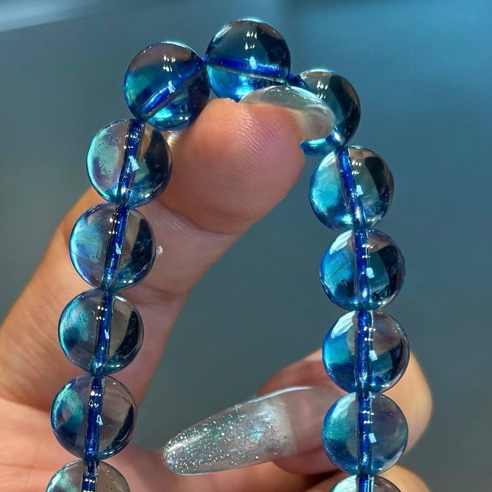 A woman's hand in a relaxed, meditative mudra pose wearing the 10.2mm aquamarine bracelet, positioning it as a tranquil energy tool under soft lighting.