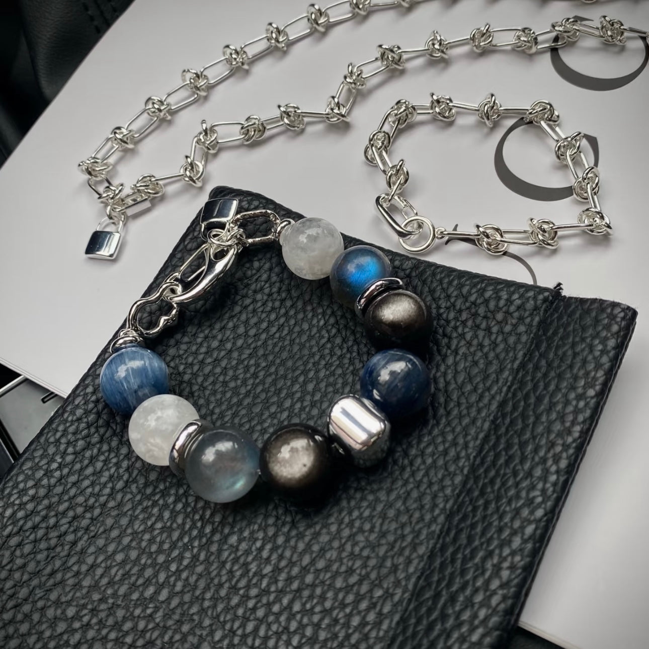Kyanite, grey moonstone and white snowflake phantom quartz crystal bracelet set with silver titanium steel bracelet, flatlay on neutral background