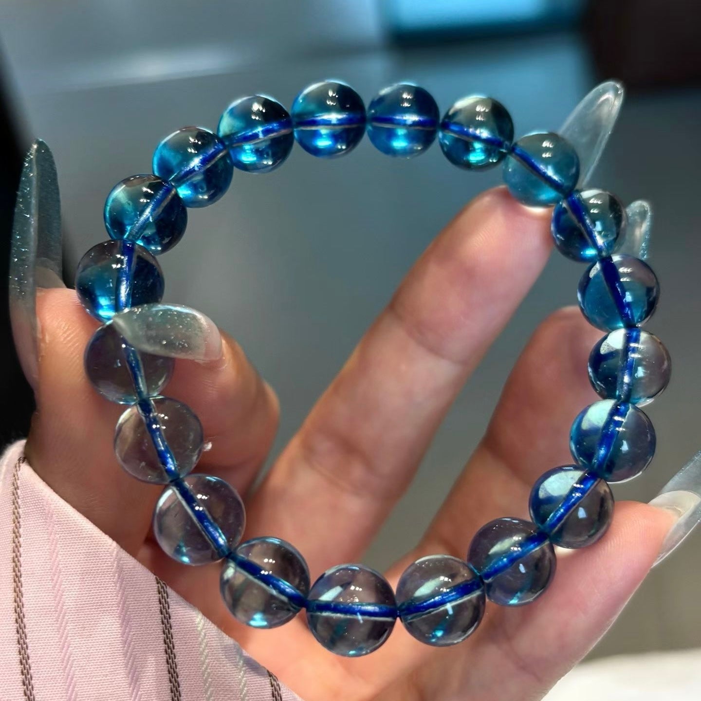 A woman's hand gently handling a single bead on a natural aquamarine bracelet, suggesting professional selection and energetic blessing in natural light.