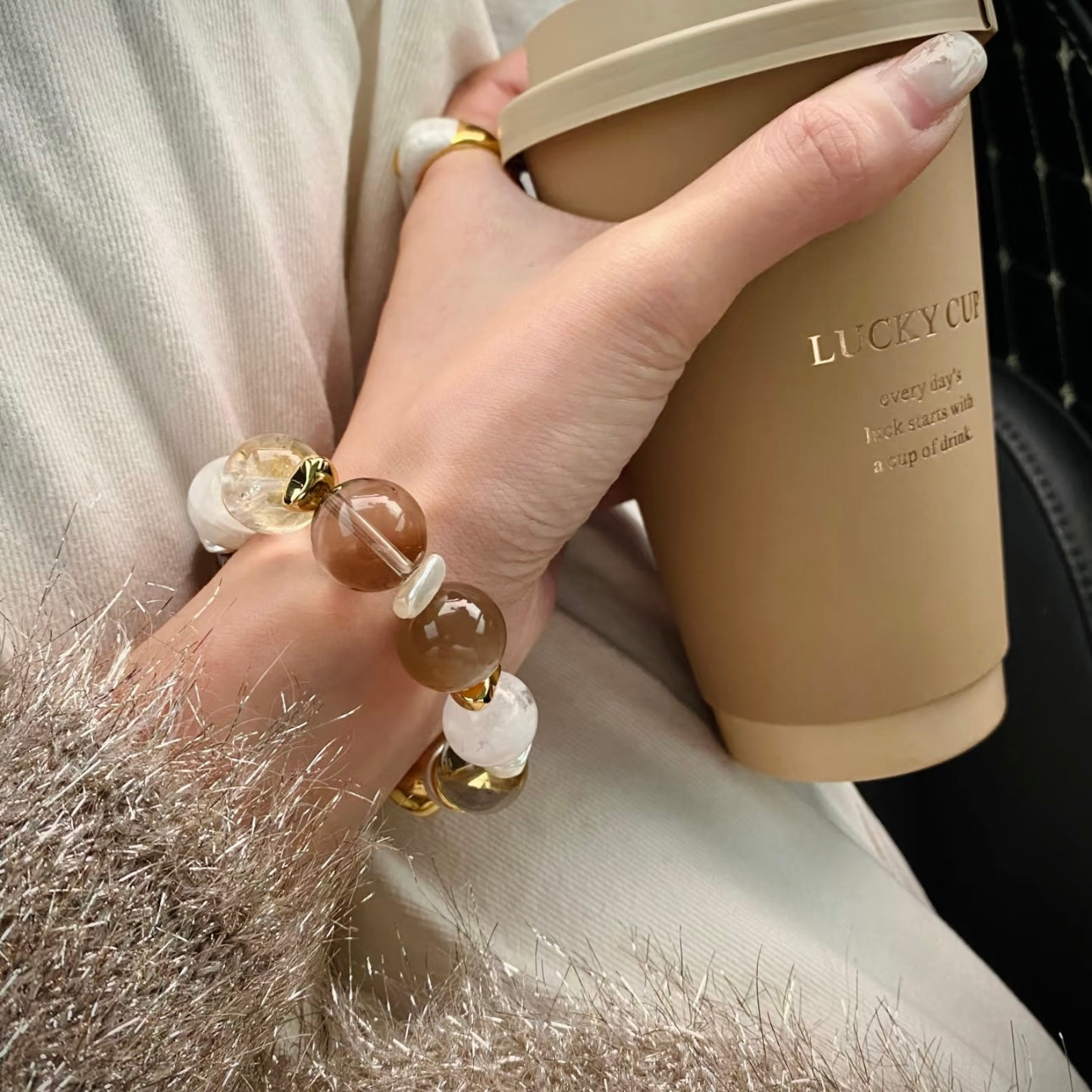 Close-up wrist shot of 14mm white snowflake phantom quartz large bead bracelet with iridescent mother-of-pearl and 24K gold titanium steel hardware