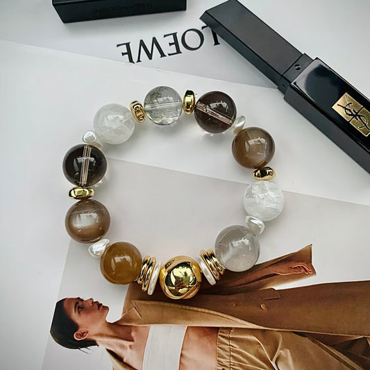 White snowflake phantom quartz and freeform mother-of-pearl crystal bracelet with milky tea moonstone and smoky quartz, flatlay on neutral background