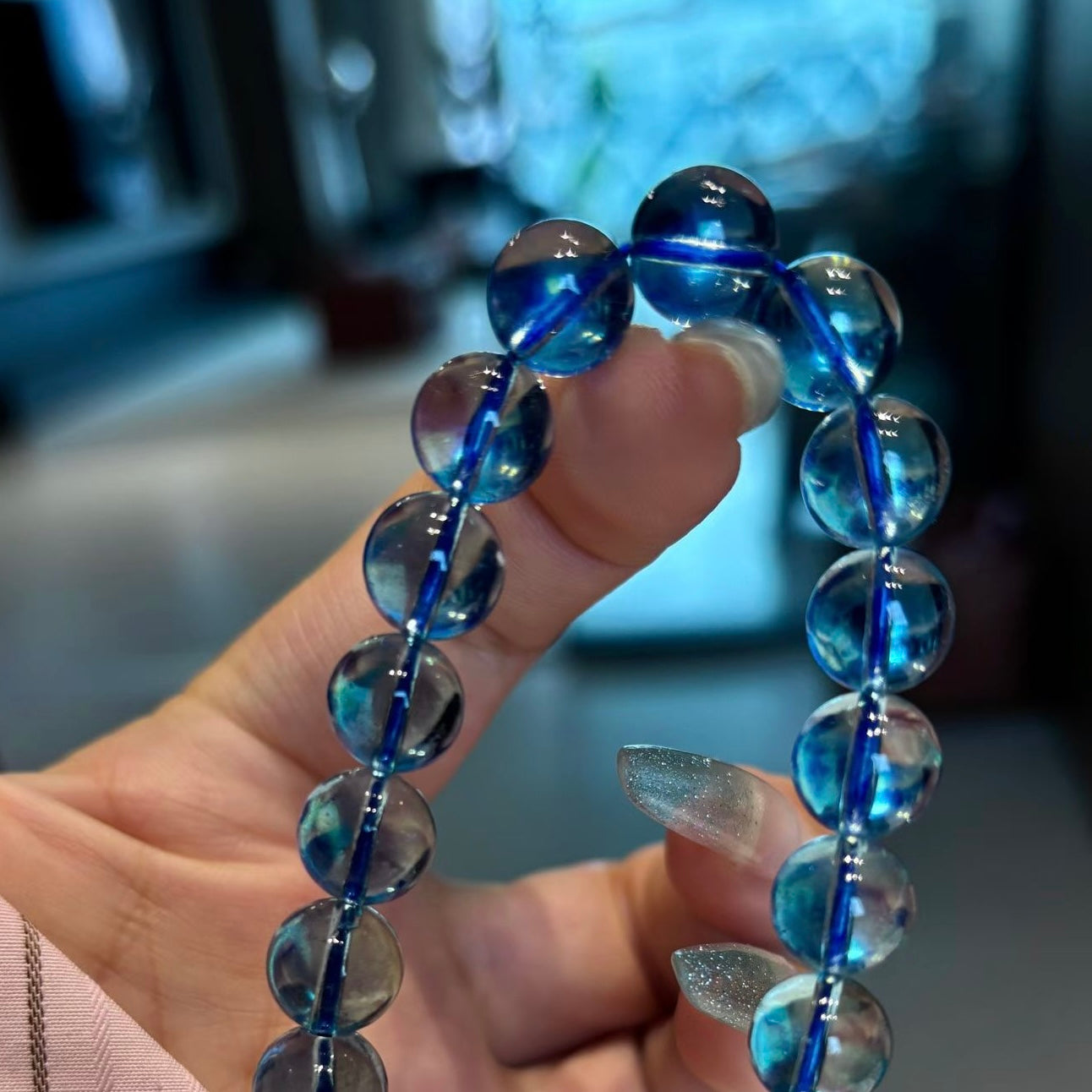 A dynamic capture of natural aquamarine beads sliding down a woman's wrist, highlighting their vibrant deep ocean blue color and the substantial 10.2mm size.