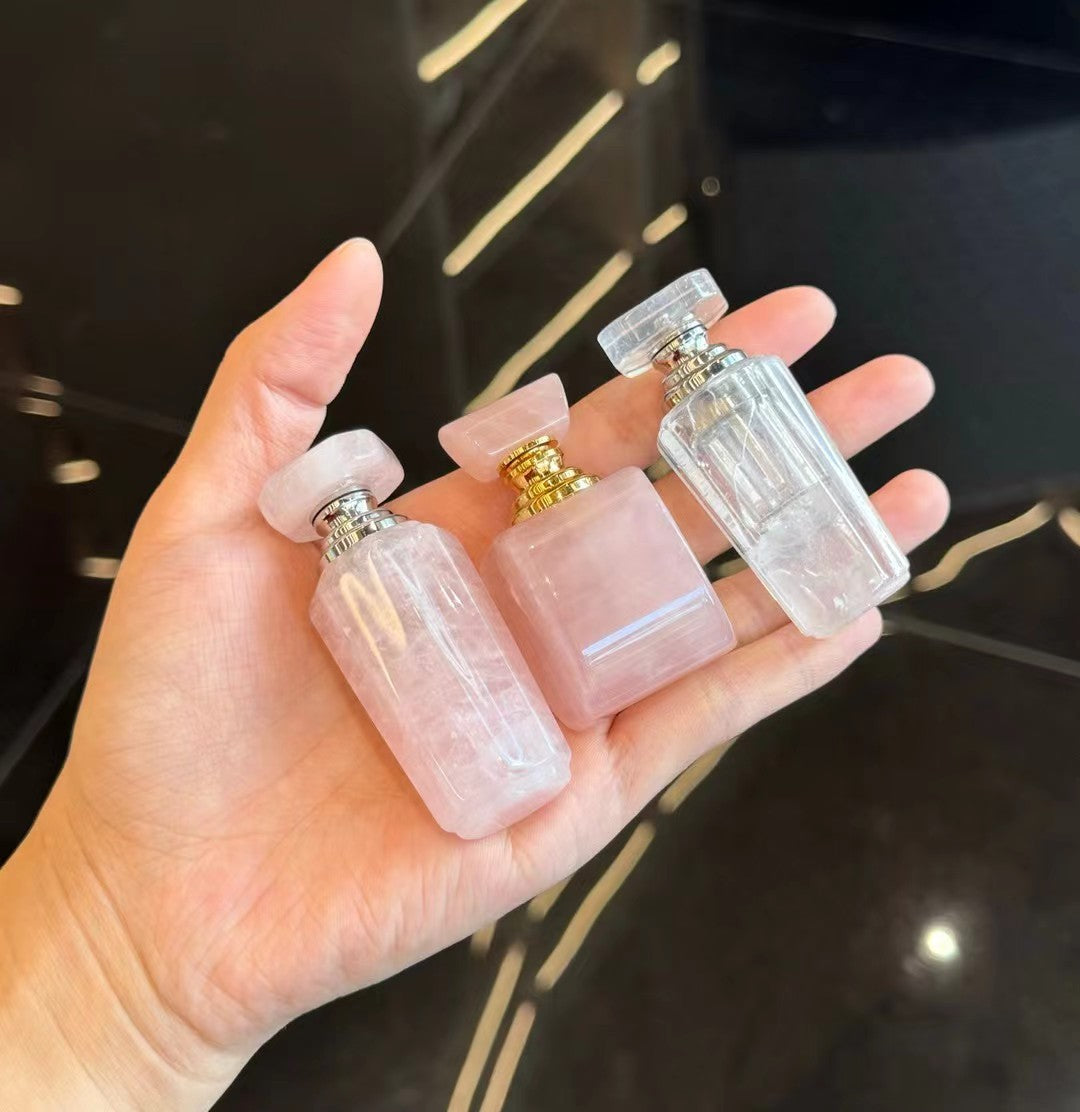 A model's hand holding three different styles of rose quartz and clear quartz bottles.