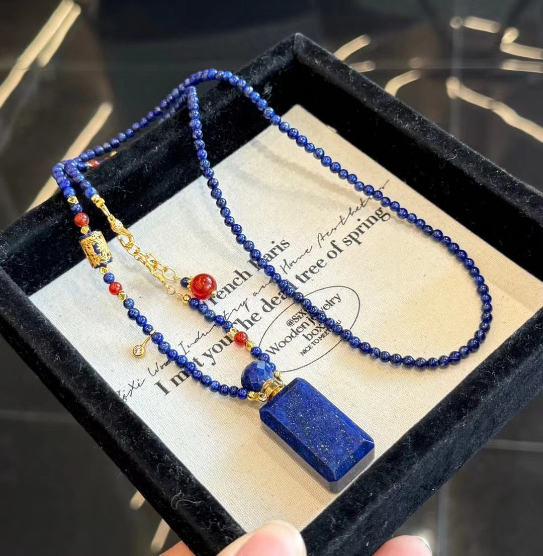 A hand touching the lapis necklace against a dark winter sweater, showing its vibrant color.