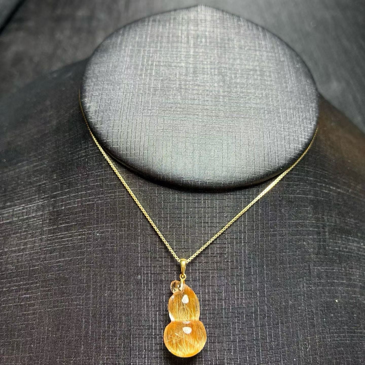 A luxury golden rutilated quartz pendant displayed on a minimalist background for elegant jewelry styling
