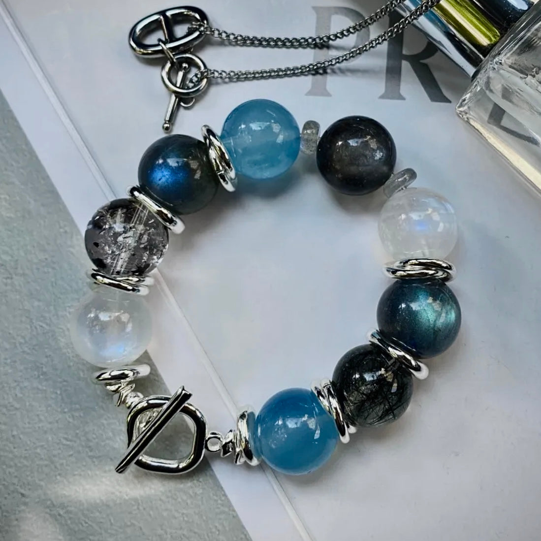 Natural Aquamarine, Moonstone, and Black Rutilated Quartz bracelet displayed in a minimalist flat lay, designed for everyday wear and modern crystal jewelry styling.