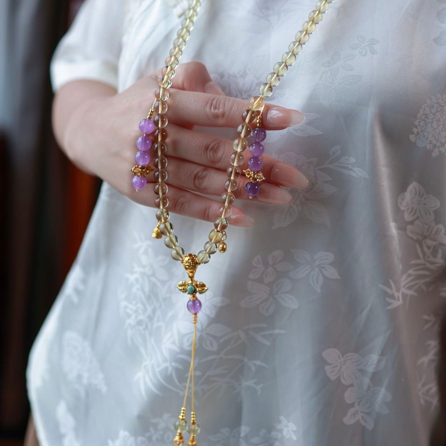 A model wearing the citrine mala necklace over a minimalist white linen outfit.