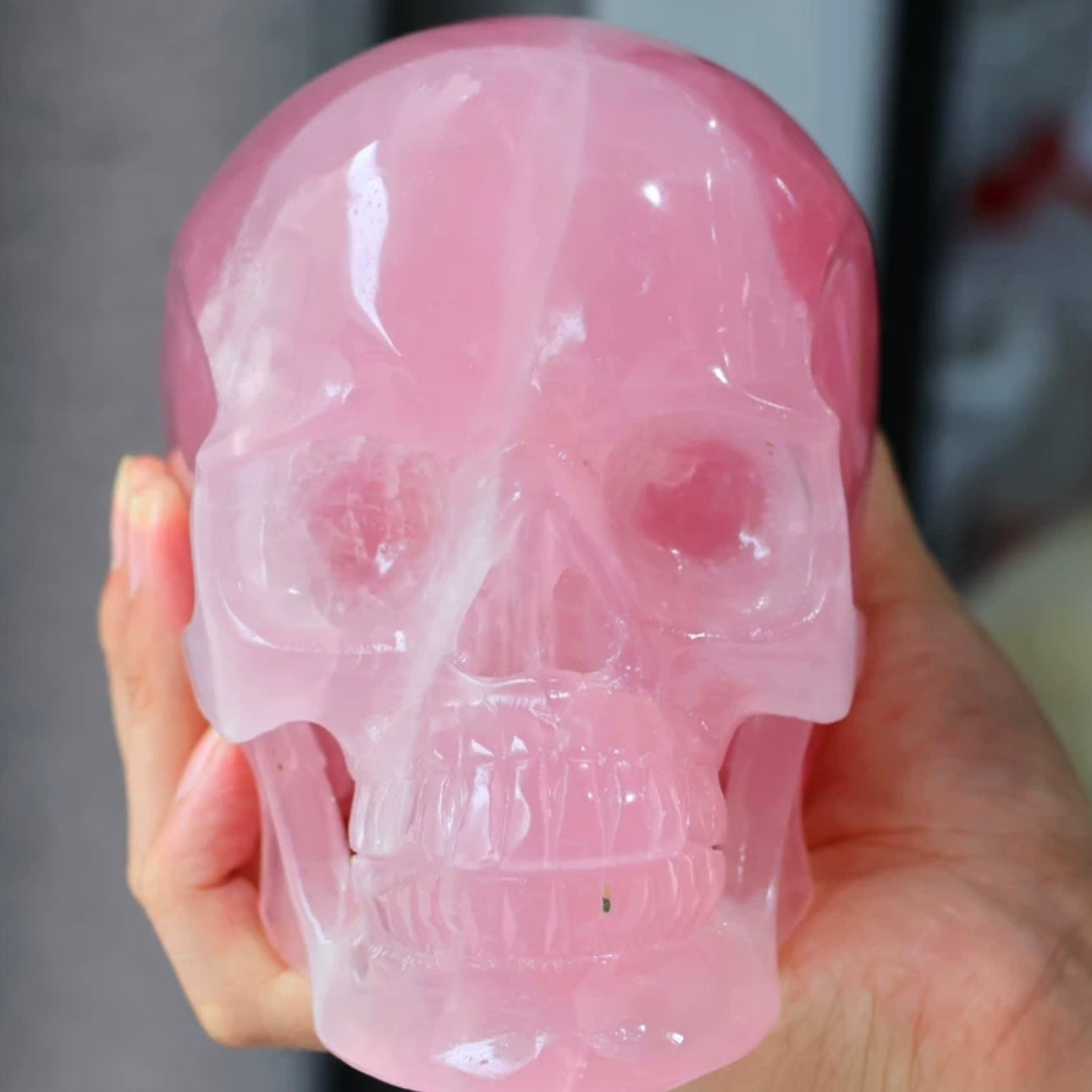 Close-up of hands holding Rose Quartz skull, highlighting lifelike carving texture and natural crystal inclusions