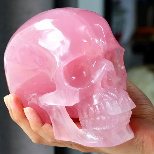 Hands holding Natural Rose Quartz Skull Carving showing front facial detail and soft pink crystal tone