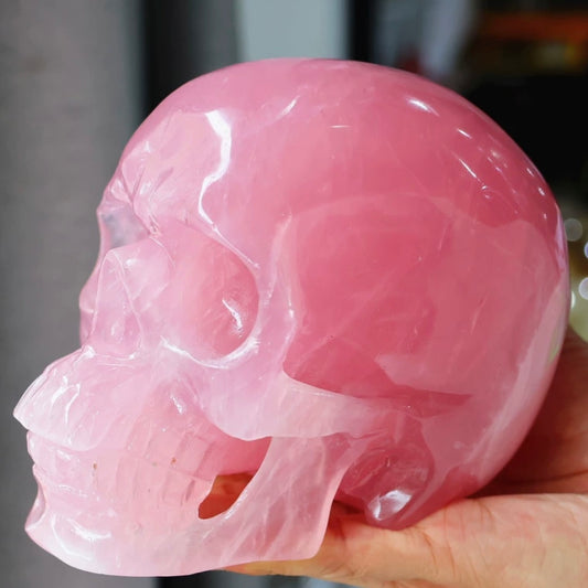 Side view of hand-carved Rose Quartz skull held in hands, revealing smooth contour and natural translucency