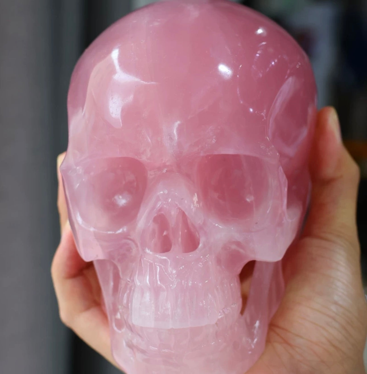 Top-down view of Natural Rose Quartz Skull Carving cradled in both hands, showing crown detail and blush pink hue