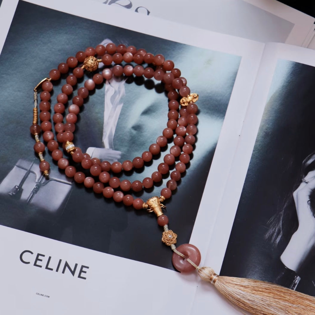 Natural 8mm Sunstone prayer beads with 925 silver gilt accessories and a tassel, shown on a fashion magazine.