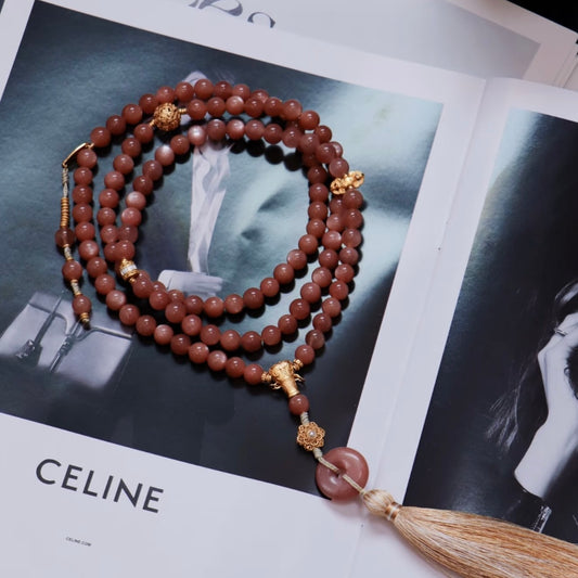 Natural 8mm Sunstone prayer beads with 925 silver gilt accessories and a tassel, shown on a fashion magazine.