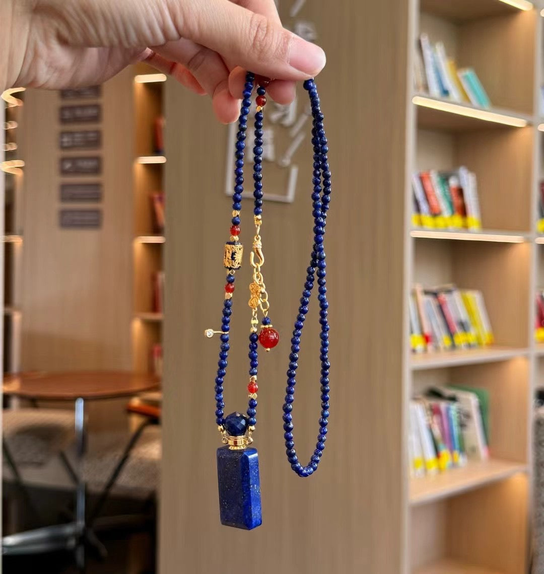 Close-up of a hand unscrewing the gold-plated cap of a lapis lazuli perfume bottle pendant.