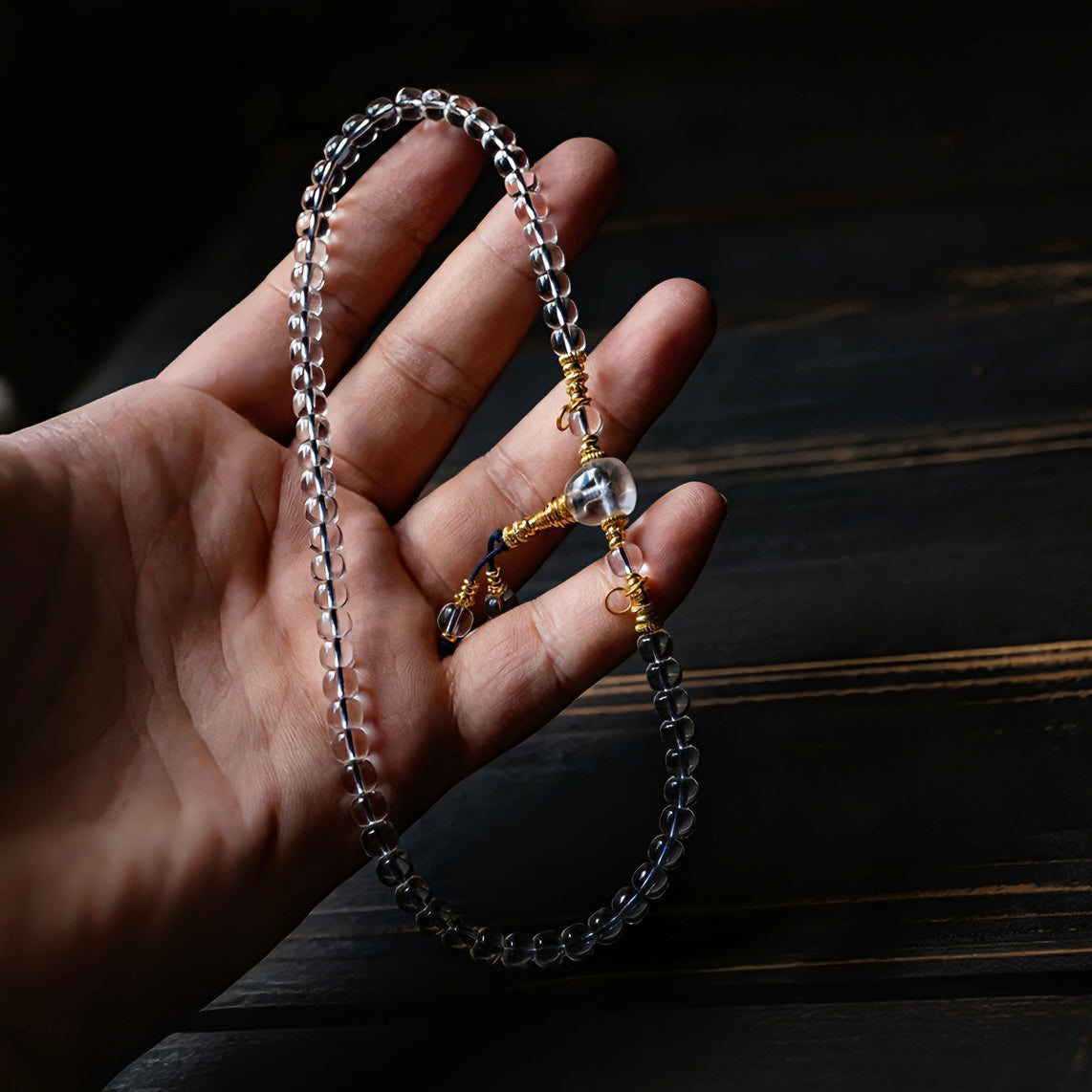 Hand stretching the crystal mala to reveal the intricately carved 24K gold-plated accents.