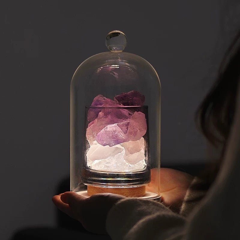 Warm orange raw crystals glowing through a glass dome held by a model.