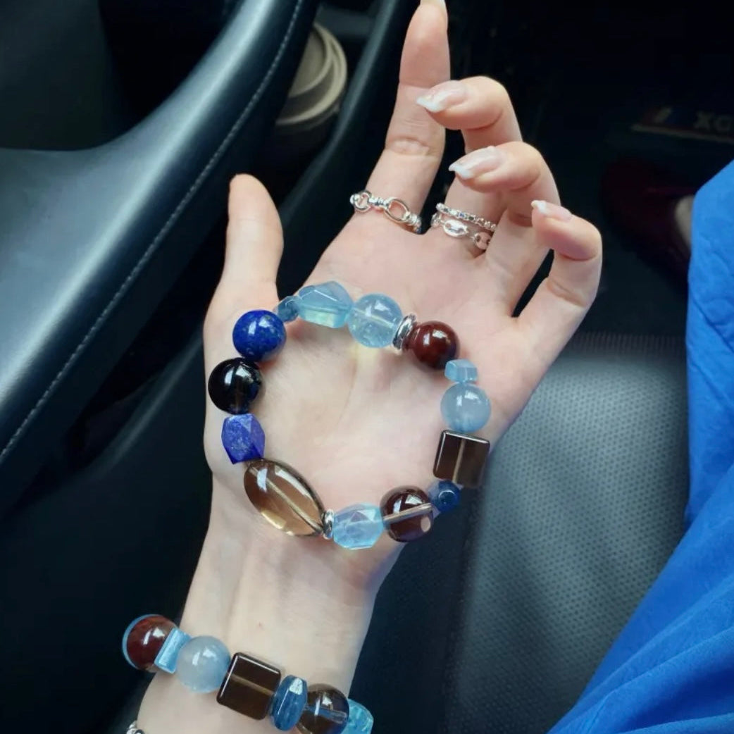 Luxury-inspired Aquamarine, Smoky Quartz and Lapis Lazuli bracelet designed to complement modern wardrobes and refined personal style, featuring Santa Maria Aquamarine, Blue Sapphire, Kyanite and artisan-cut gemstone details. Includes complimentary matching Lapis Lazuli earrings with bracelet purchase.
